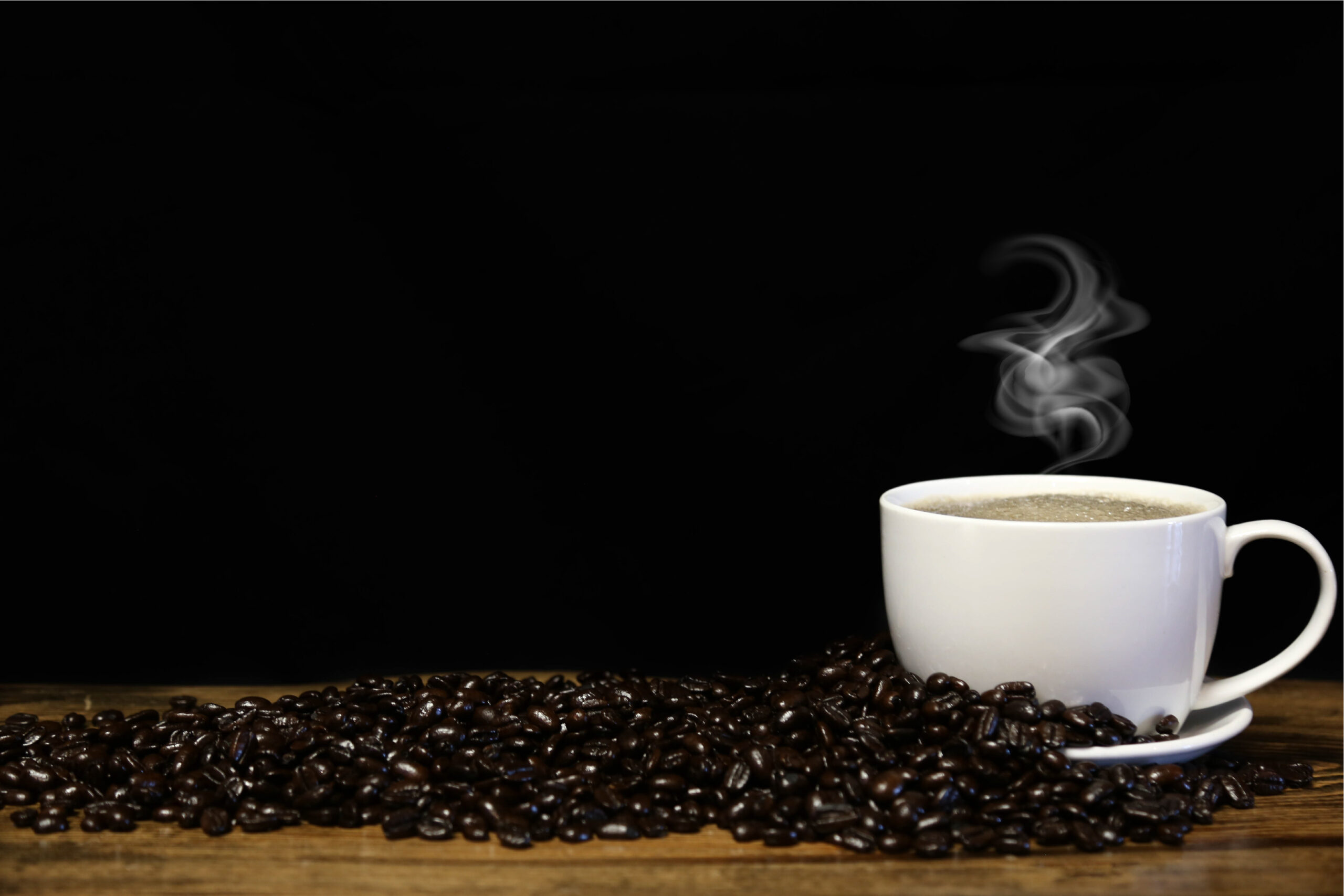 A steaming cup of coffee beside a pile of roasted coffee beans